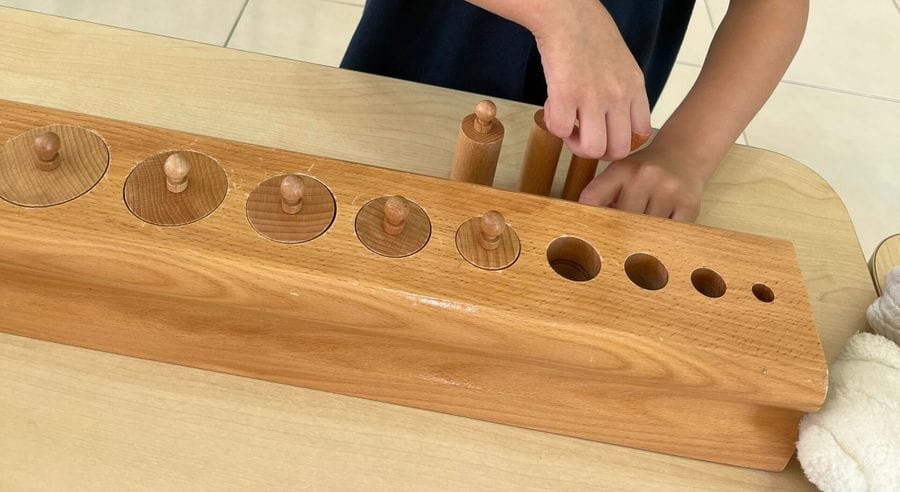 A child placing wooden knobbed cylinders in a Montessori block