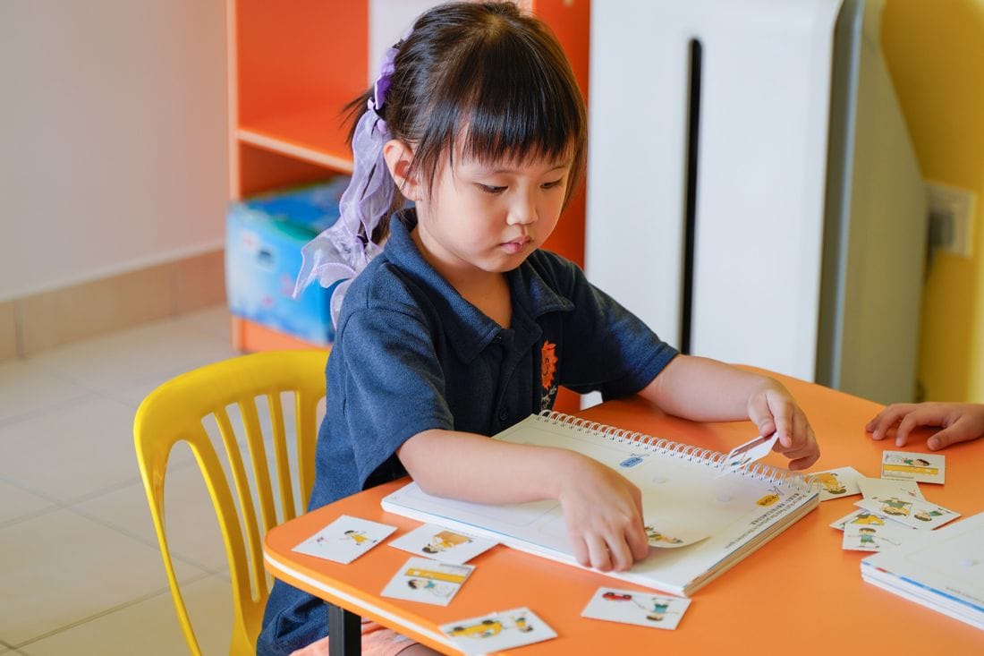 A kindergarten child matching picture cards in a workbook